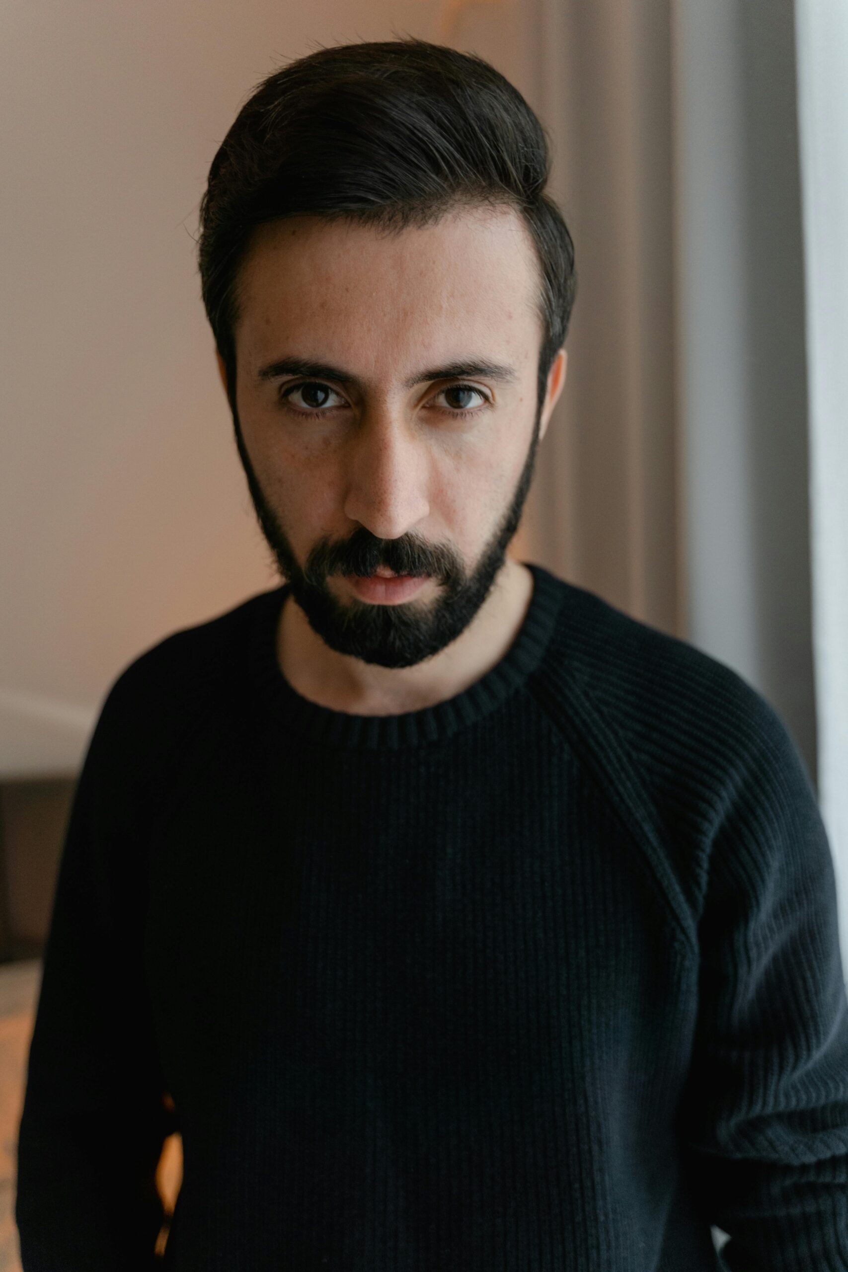 Portrait of a bearded man in a black sweater with a thoughtful expression.